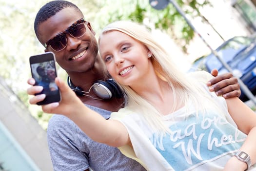 Young laughing multicultural couple take photo with smartphone mobile phone in summer