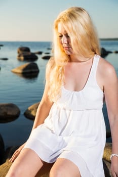 Woman in white dress taking sun on stone