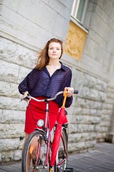 Self-confident woman in red skirt next to bicycle