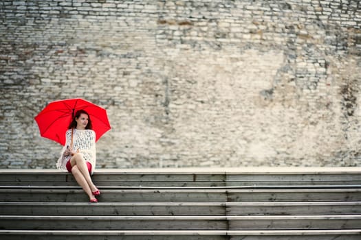 Happy woman sit with open umbrella at steps