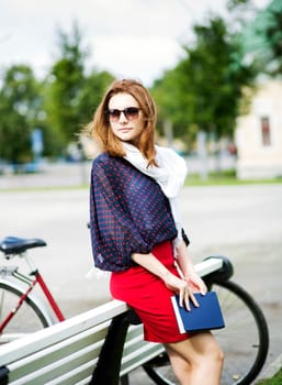 Attractive woman rests on bench and hold book