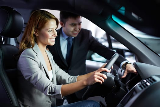 Photo of young woman sitting in car while being consulted by salesman in automobile center