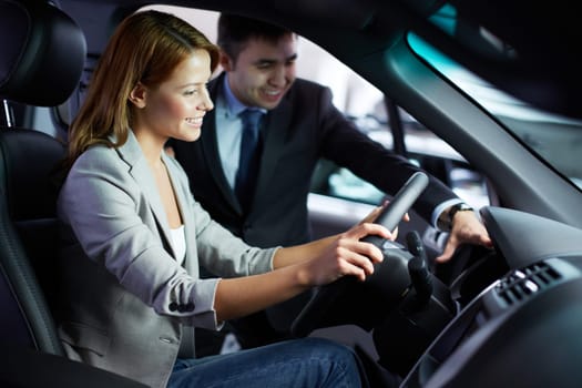 Photo of elegant woman sitting in car and listening to salesman in automobile center