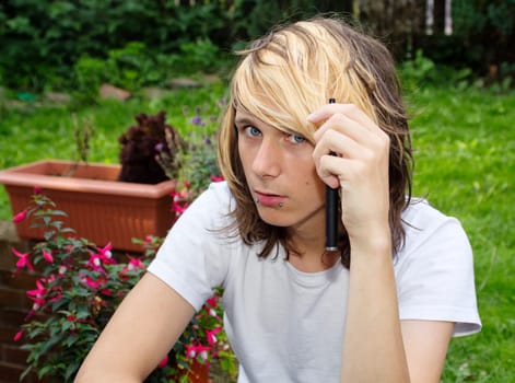 Teenage boy holding an electronic cigarette, and looking directly to camera. The look in his eyes could mean several different things.