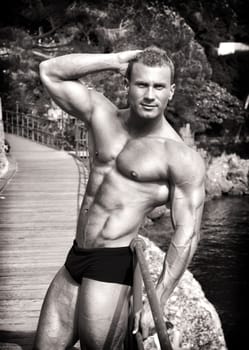 Sepia portrait of attractive young muscle man outdoors showing muscular body with hand behind his head