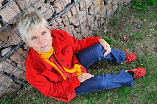 elderly woman with red jacket sits on the floor with a view from above  mature woman with red jacket sitting on the ground  down view