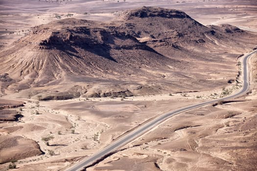 Stony desert landscape with road and acacia trees, Morocco.