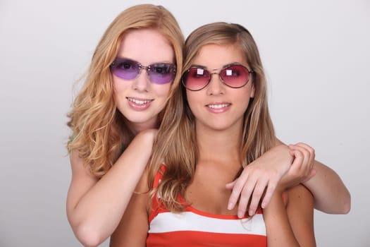 Studio shot of two pretty teenagers wearing colored sunglasses