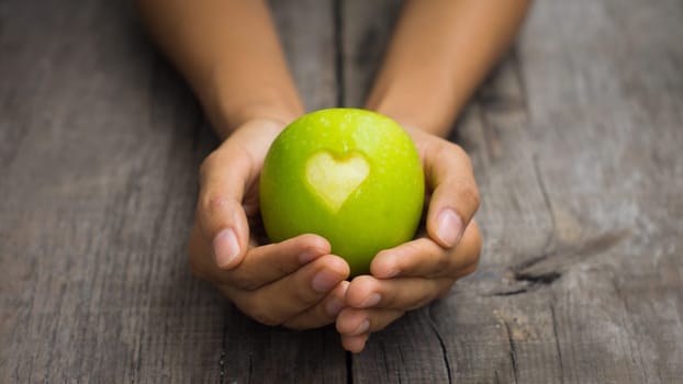 A person holding a Green Apple with engraved heart