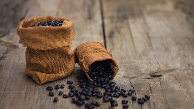 Small bags with black beans on wooden background