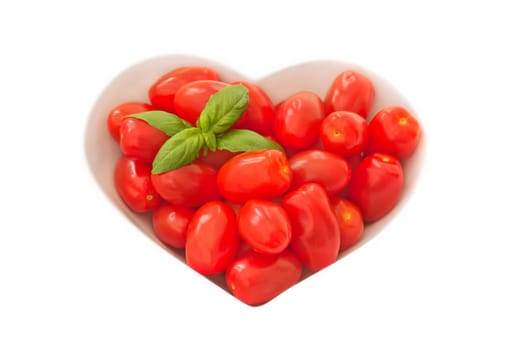 A bowl of baby plum tomatoes on a light coloured cloth. there is a sprig of basil in the top left hand corner to give a splash of green.