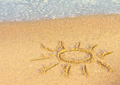 Drawing of the sun on sand with sea wave