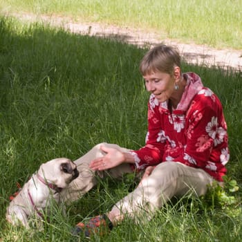 Full body view of an elderly woman with dog (pug) and view of the dog sitting in the grass in summer