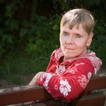 Portrait of an elderly woman on a park bench in summer with her upper body turned backwards over her backrest towards the camera