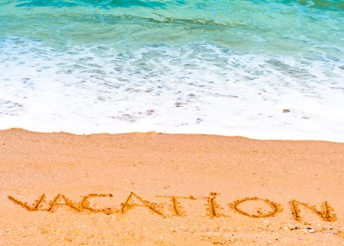 Vacation word written in the sand on the beach with  blue waves in the background