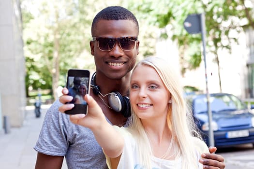 Young laughing multicultural couple take photo with smartphone mobile phone in summer