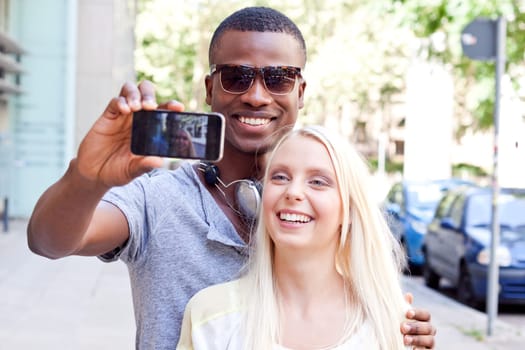 Young laughing multicultural couple take photo with smartphone mobile phone in summer