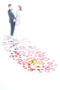 Pure gold wedding rings with red hearts ornament and wedding couple at the background