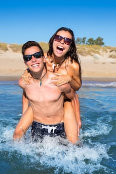 Teen couple enjoying  piggyback on summer beach shore splashing water