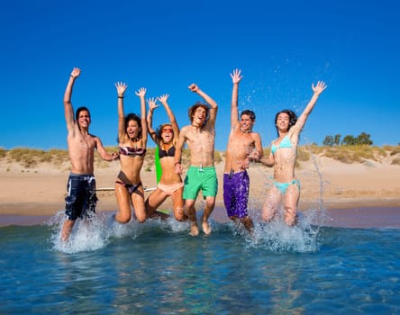 Happy excited teen boys and girls group jumping at the beach splashing water