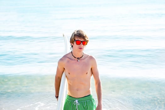 Boy teenager with surfboard on beach shore and orange sunglasses