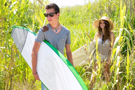 Surfer boy and girl walking in the green jungle with sunglasses