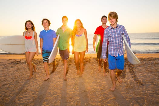 Surfers teen boys and girls group walking on beach at sunshine sunset backlight