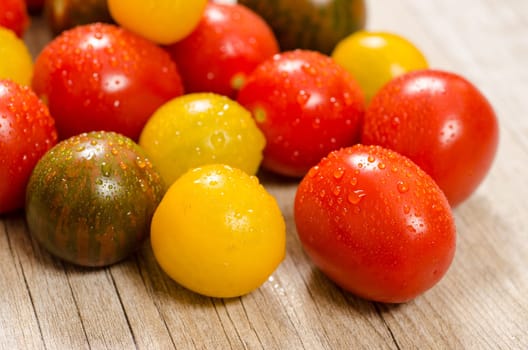 Colorful wet cocktail tomatoes with drops of water on a wooden board