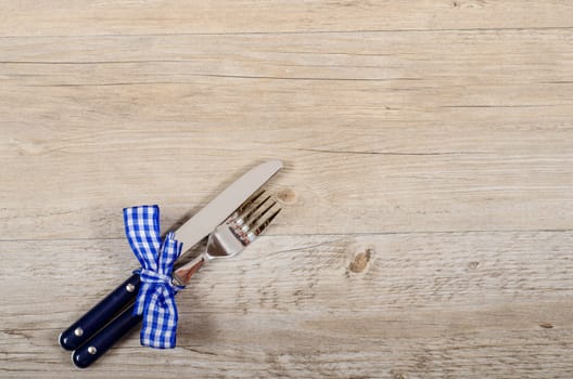 Blue knife and fork with checkered bow on a wooden table