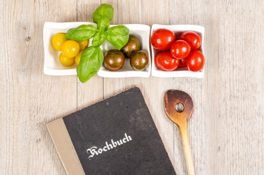 Cookbook and cooking spoon with tomatoes and basil as an ingredient