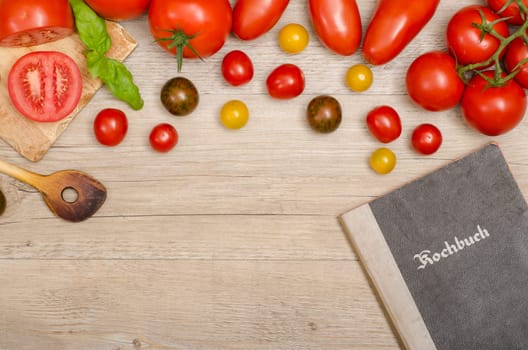 Frame made of different tomatoes,cooking spoon and cookbook on old wood