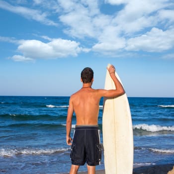 Boy surfer back rear view holding surfboard on blue beach