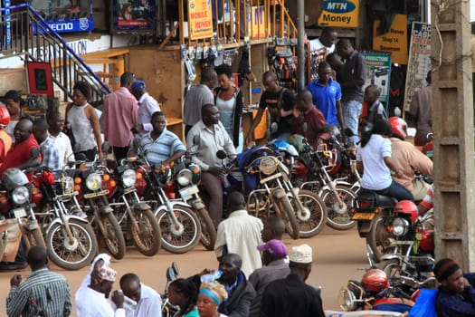 KAMPALA, UGANDA - SEPTEMBER 28, 2012. Motorcycle taxis and drivers wait on the streets for passengers as people walk by in Kampala, Uganda on September 28,2012.