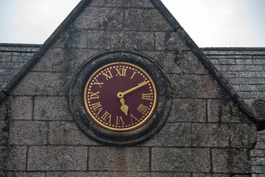 A Vintage Red and Gold Clock with roman numbers on a stone built building
