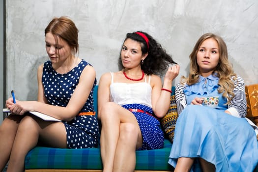 Three womans in different dresses sit on sofa