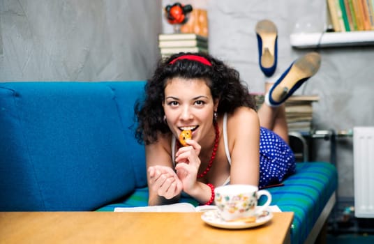 Woman lay on soft sofa and eat biscuit