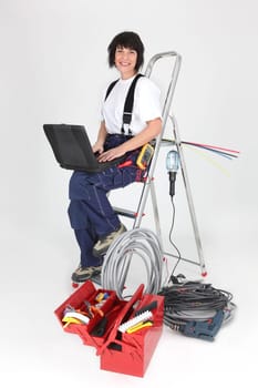 Woman electrician sitting on a ladder with laptop