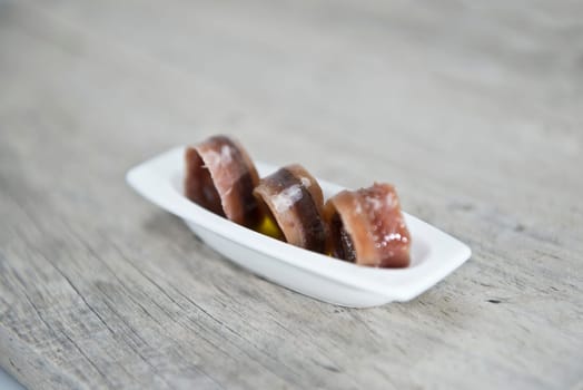 Anchovy appetizer served in a china spoon on a wooden background