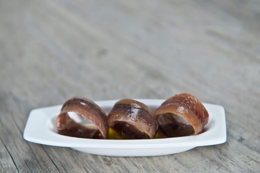 Anchovy appetizer served in a china spoon on a wooden background