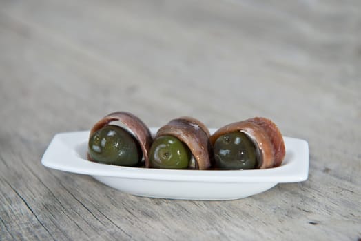 Anchovy appetizer served with green olives in a china spoon on a wooden background
