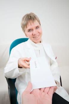 elderly woman sitting on a chair in a white doctor's coat receives an envelope with an application letter from the direction of the camera from one hand
