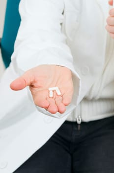 on the hand of an unrecognizable seated woman lie three medicine capsules