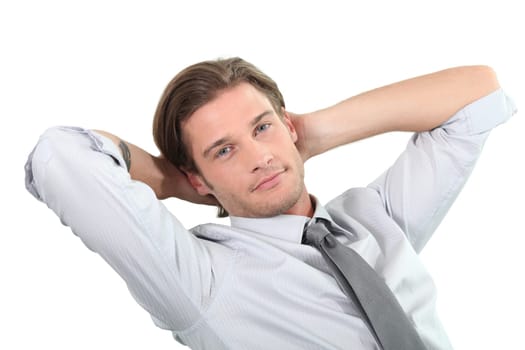 Young businessman sitting with arms behind head.