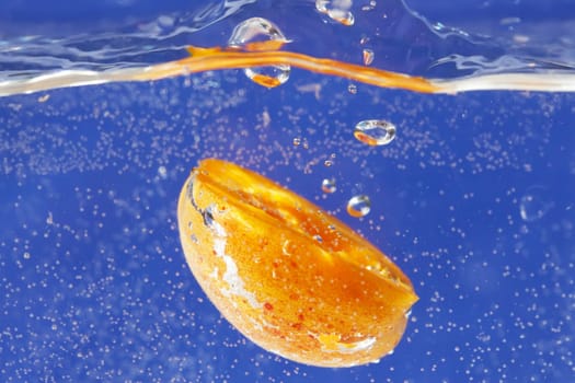 Close-up view of a apricot thrown into the water. Blue background.