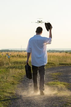 Man with a hat walks under a landing plane and greets