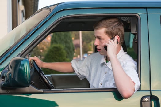 A young man sits in the car and makes phone calls