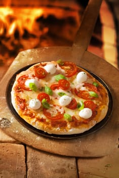 High angle view of an uncut crusty Italian pizza with cheese and tomato topped with mozzarella and fresh basil