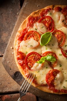 Overhead view of an appetizing tomato pizza with golden melted cheese and basil served on an old wooden board