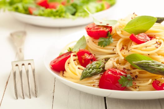 Vegetarian spaghetti pasta with fresh green asparagus spears, tomato and herbs served with a leafy green salad