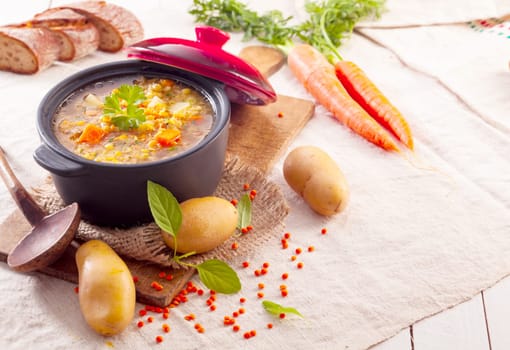 Delicious thick vegetable stew or soup in a pot surrounded by scattered fresh vegetables and ingredients in a rustic kitchen